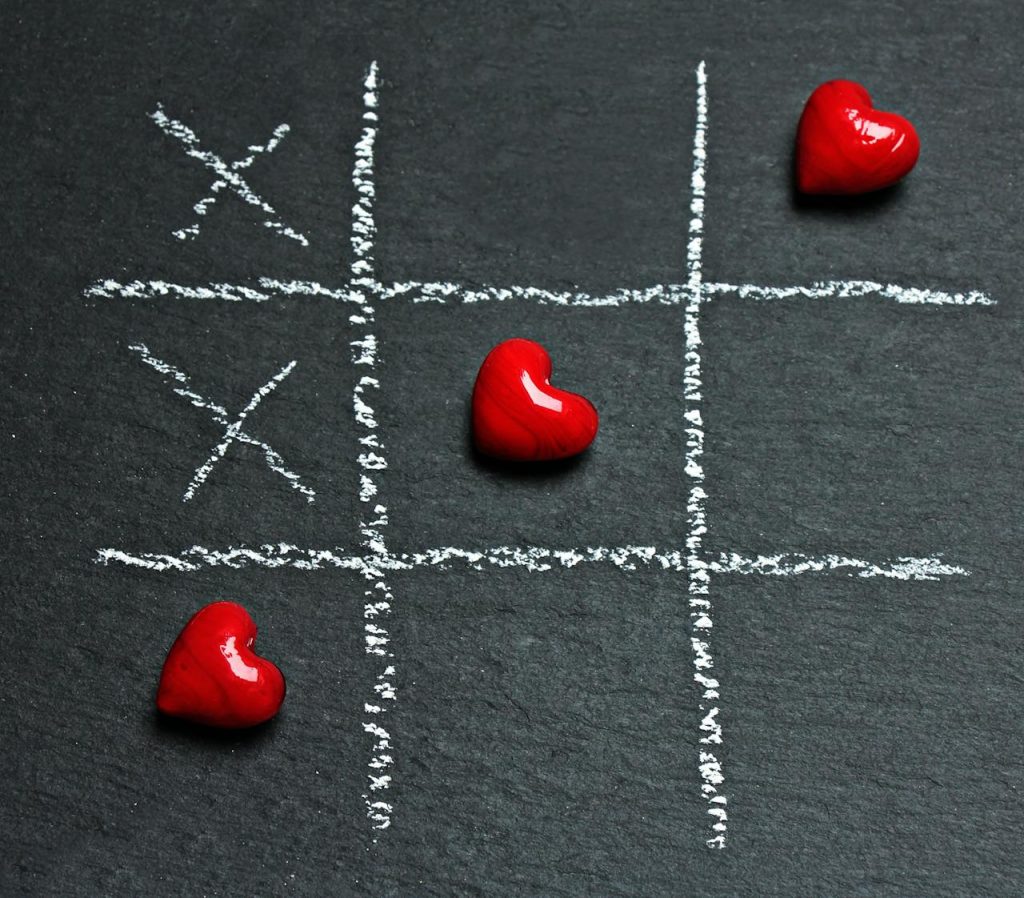Chalkboard tic tac toe game with red heart shapes symbolizing love and strategy.